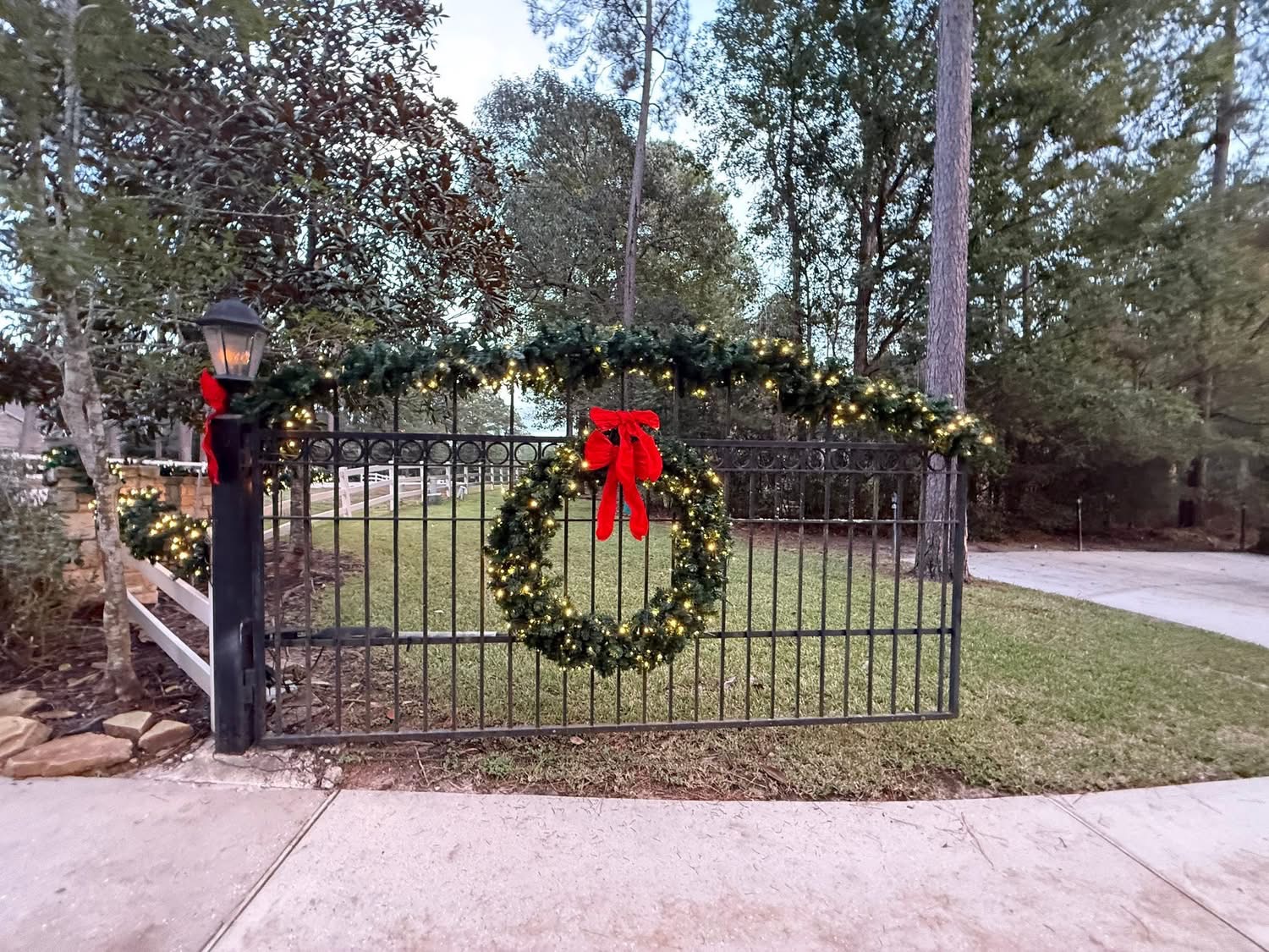 Iron entry gate dressed with lit Christmas garland and a wreath with a red bow