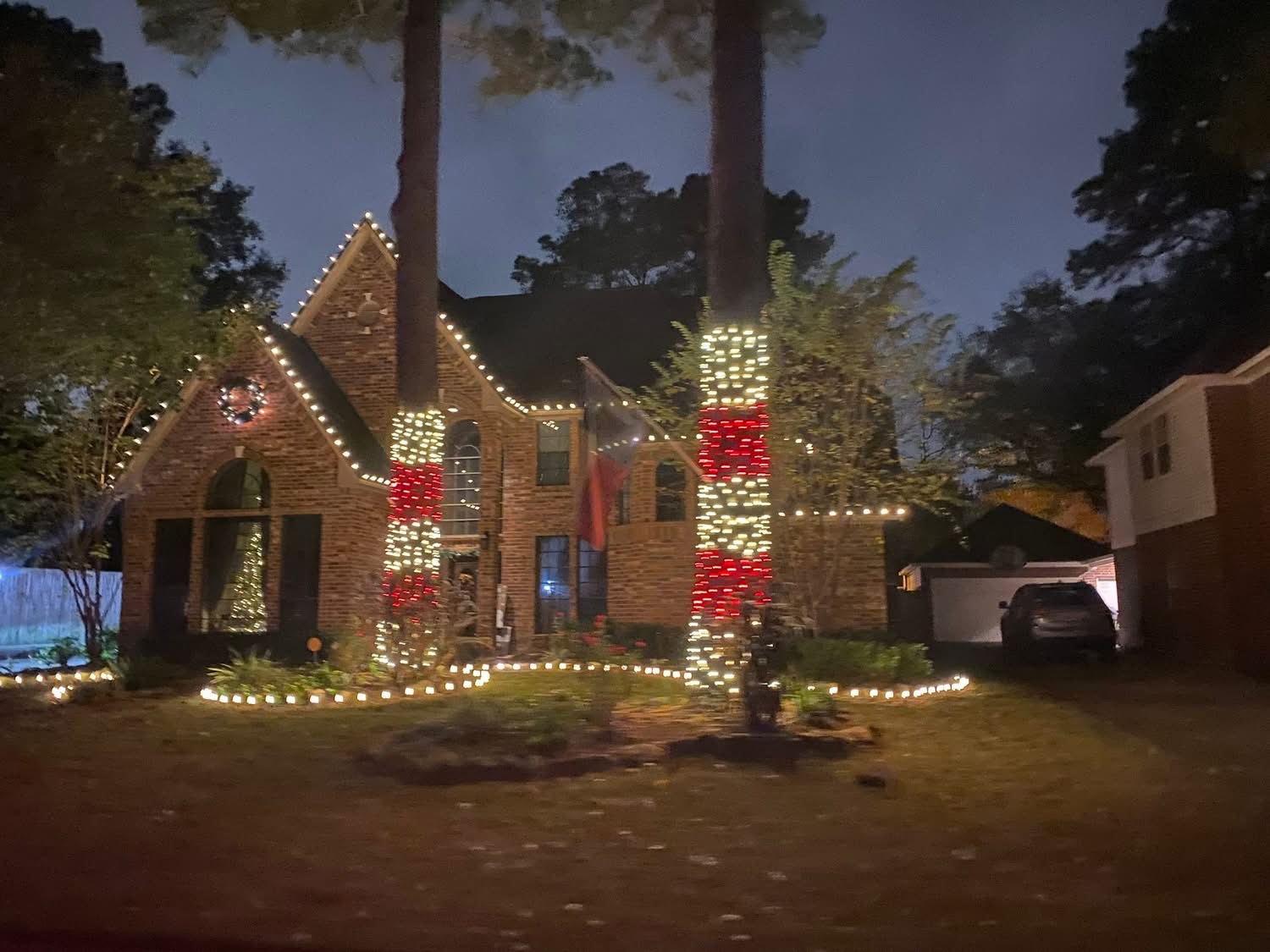 Brick home with candy-cane red and white wrapped trees and warm roofline lights