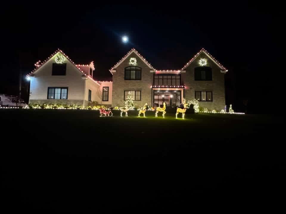 Large home with warm white roofline lights, wreaths, and lit reindeer figures on the lawn