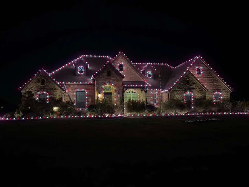 Sprawling brick home outlined in red and warm white Christmas lights with lit windows