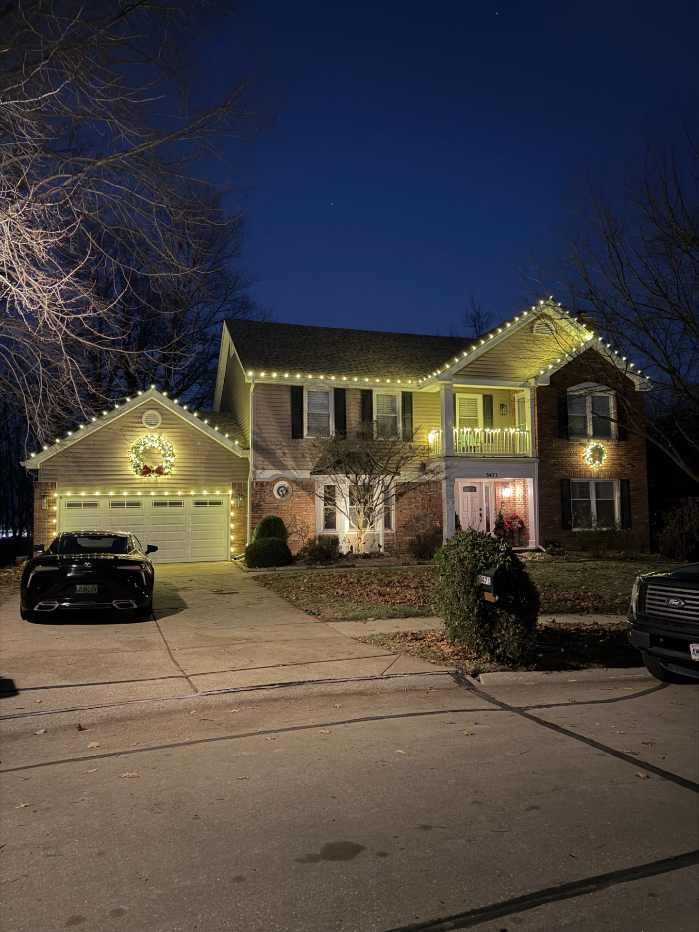 Two-story home with warm white roofline lights and lit wreaths on the garage
