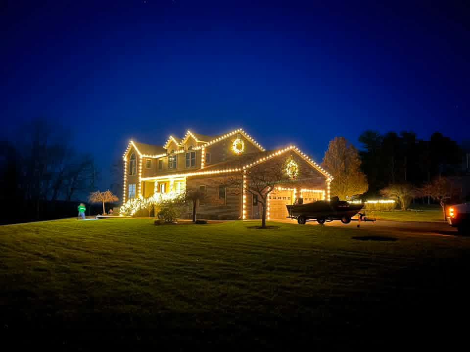 Two-story home glowing with warm white Christmas lights and lit wreaths at dusk