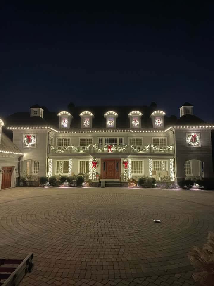 Grand estate home with warm white Christmas lights, balcony garland, and wreaths on every window
